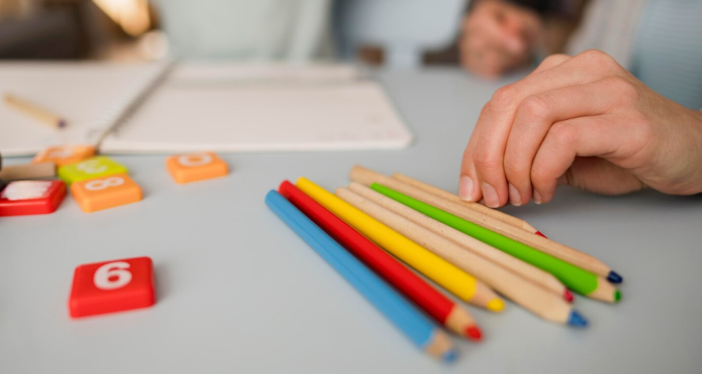Close-up of a workspace showing colored pencils, number blocks, and a notepad, illustrating the foundational tools used in early education.