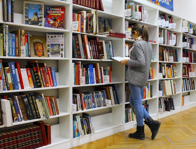 A student woman stands before a bookshelf, surrounded by a collection of book